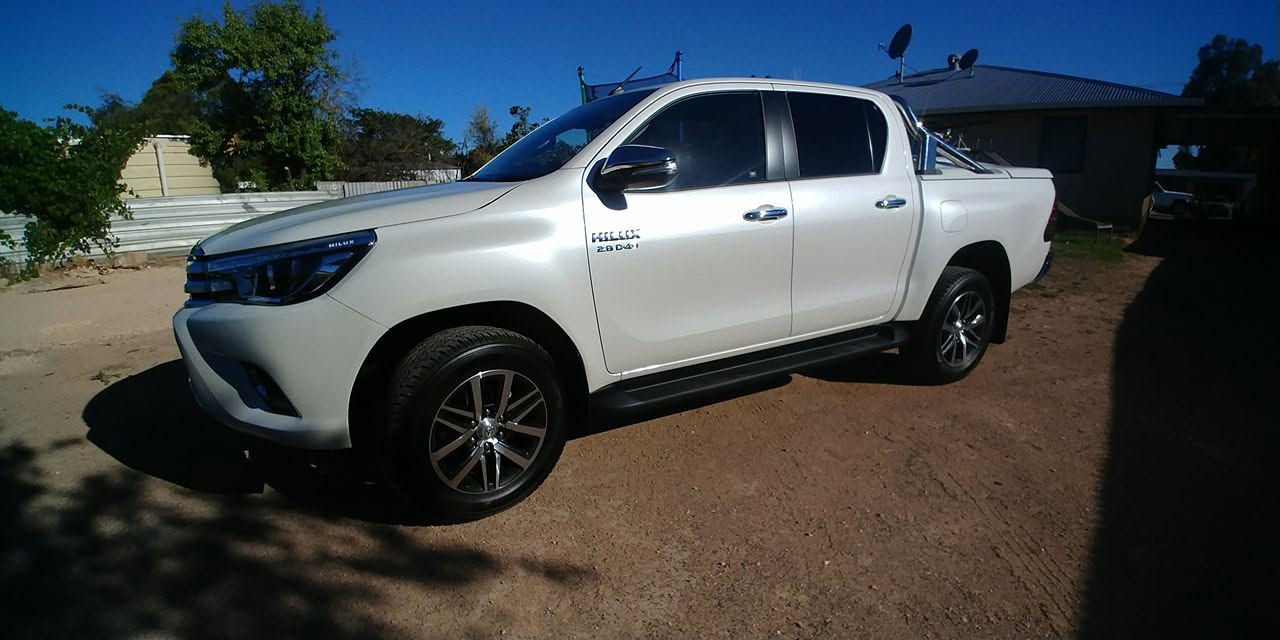 A white Toyota Hilux 4WD parked on red dirt under a clear blue sky